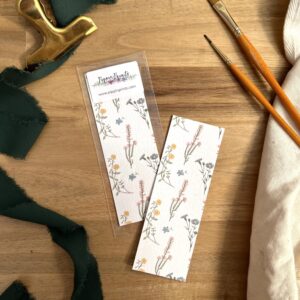 Photograph of Wildflower Pattern Bookmark by Pippin Prints shown both with and without packaging and surrounded by a dark green ribbon and paint brushes.